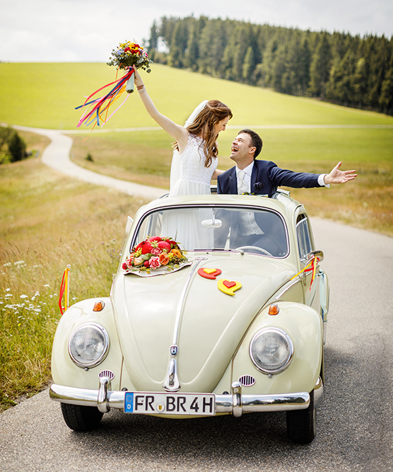 Jubelndes Brautpaar im Hochzeitsauto