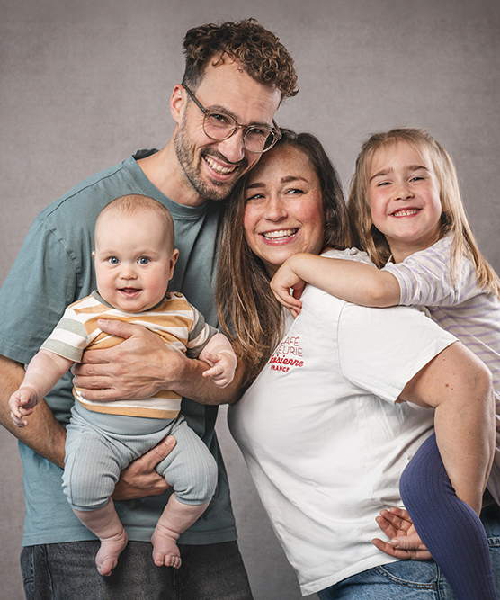 Familienbild im Fotostudio mit Baby auf Papas Arm und ein Mädchen auf Mamas Rücken